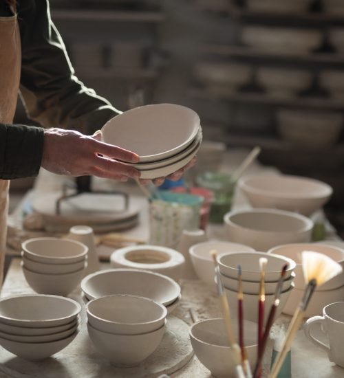 Mid section of male potter holding bowls in pottery workshop